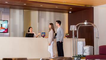 A hotel reception area with a reception desk, a television screen, and a luggage cart.