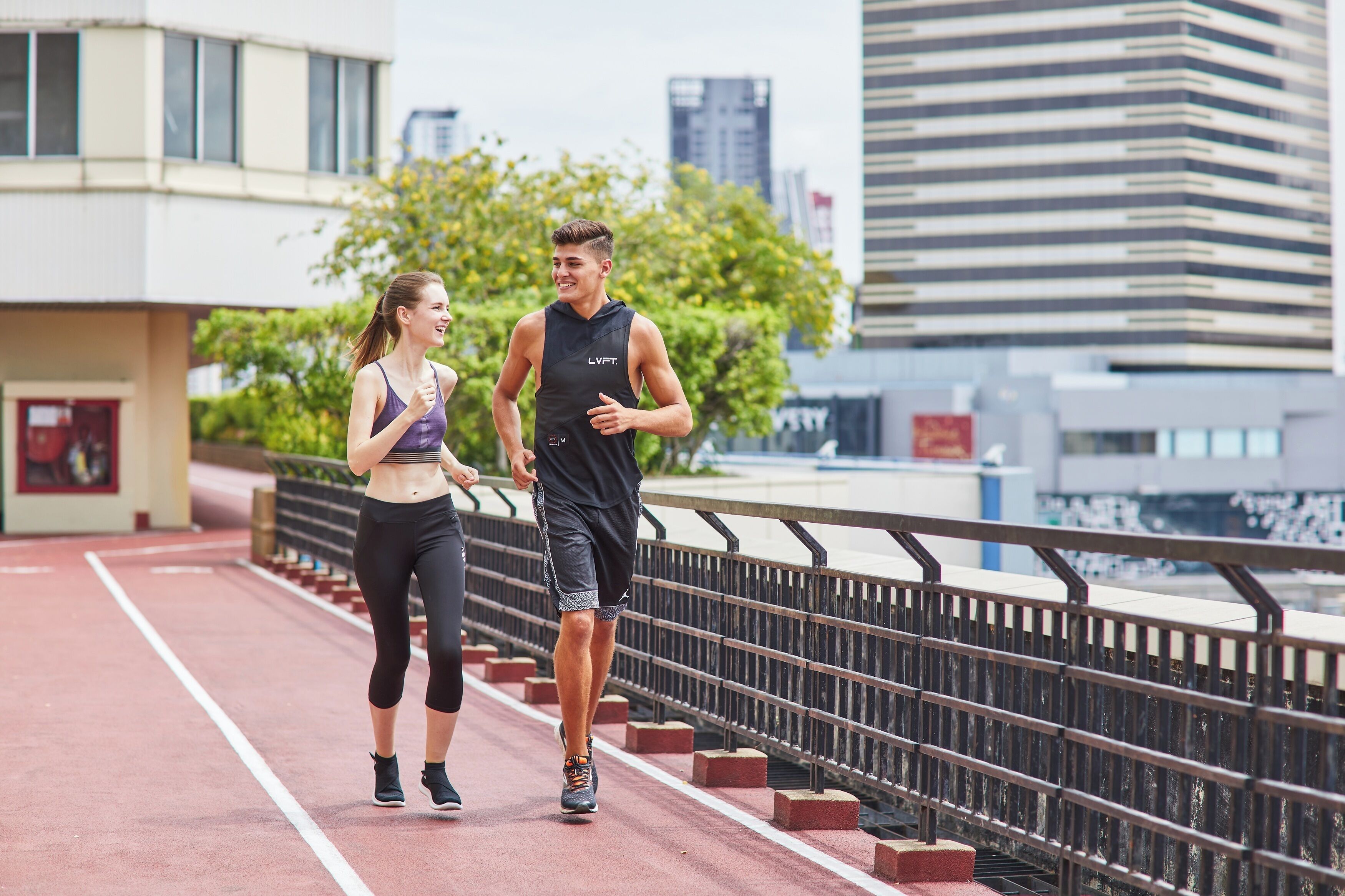Two people jogging on a red track with a cityscape in the background.