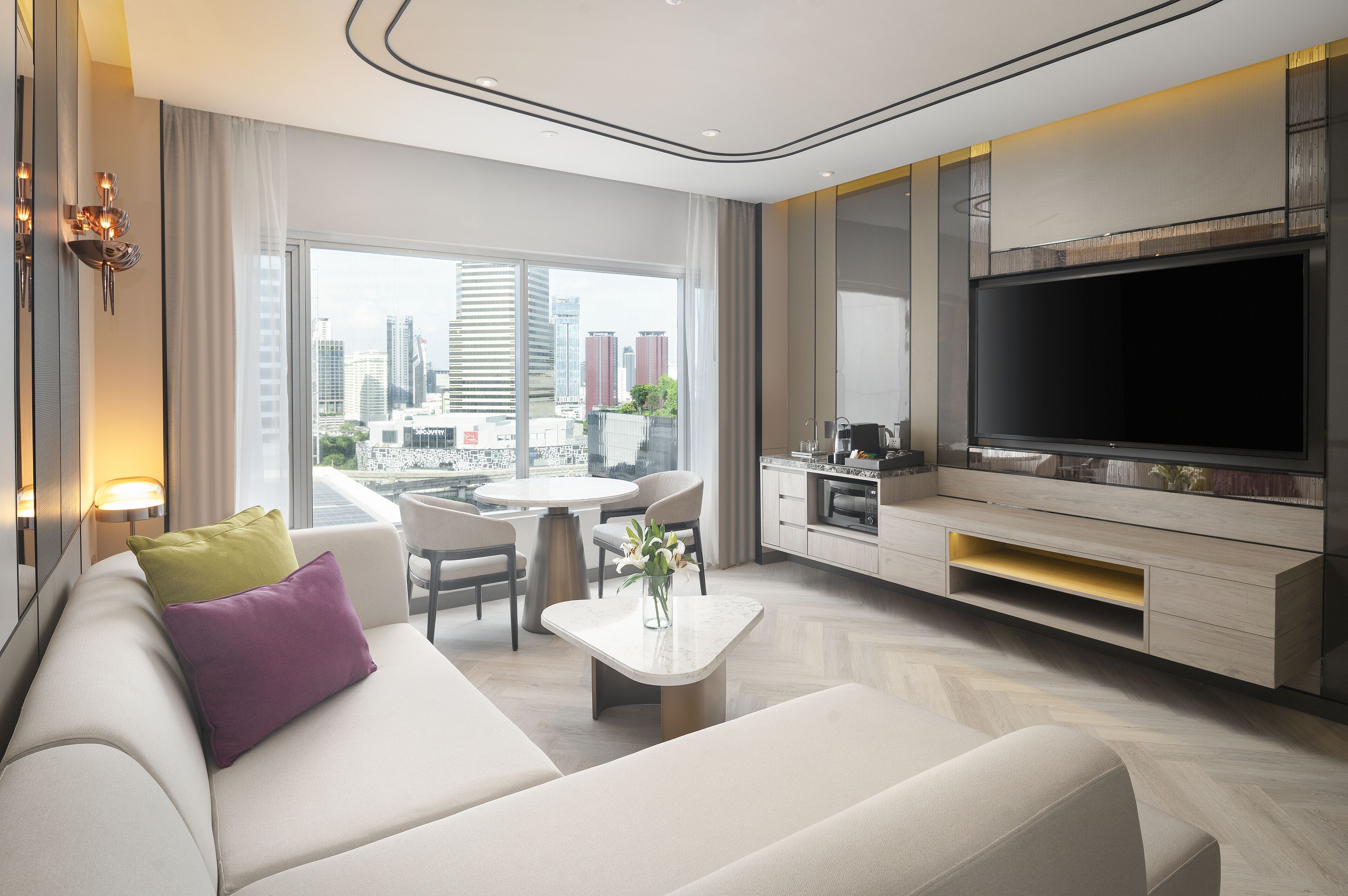 Una sala moderna con un televisor grande, un sofá, una mesa de comedor y vistas de la ciudad.