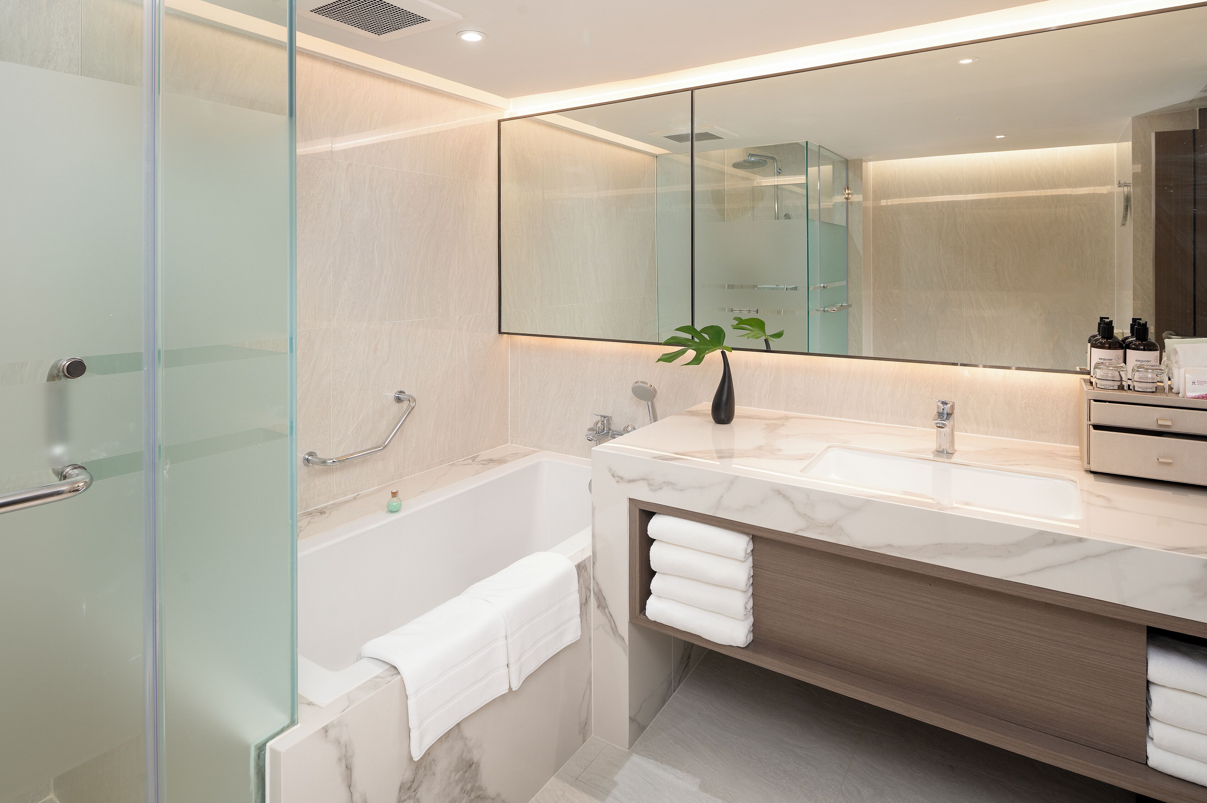 A modern bathroom with a glass shower enclosure, a freestanding bathtub, a large mirror, and a marble countertop.