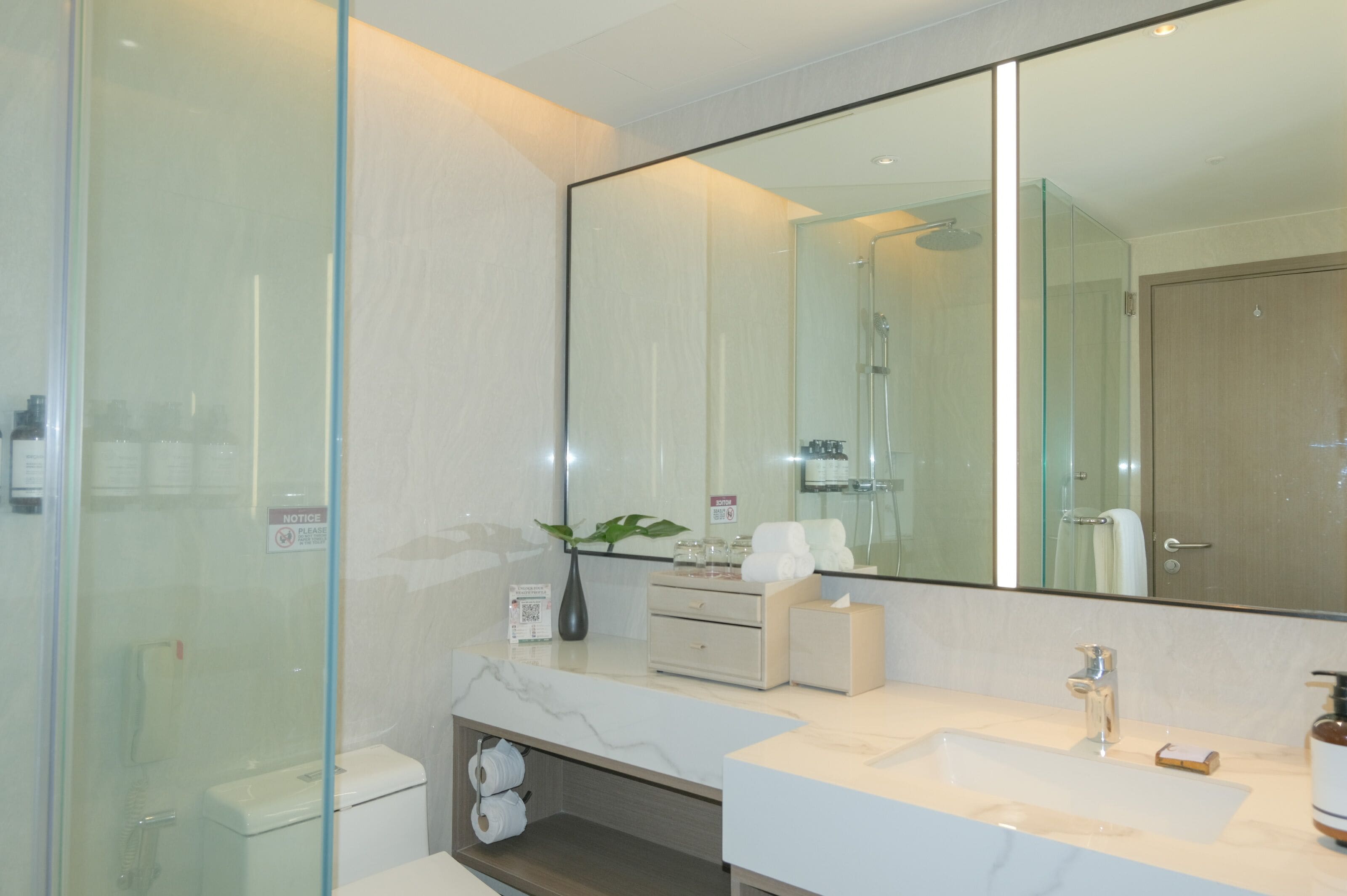 A modern bathroom with a large mirror, a glass shower enclosure, a marble sink, and a toilet.