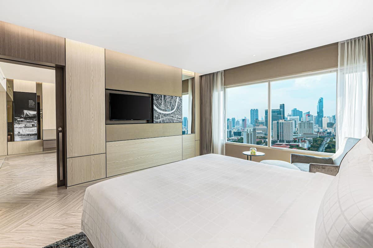 A hotel room with a large bed, a TV, a city view, and a modern design.