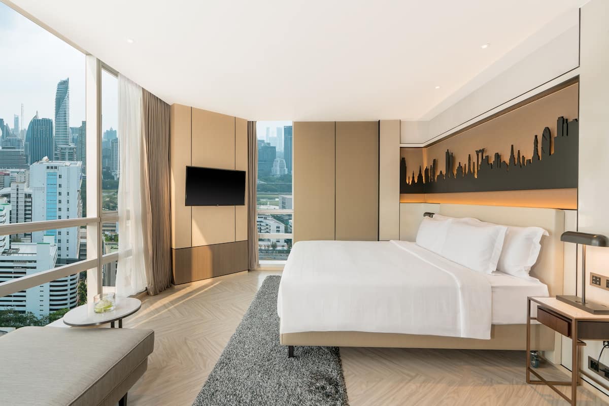 A modern hotel room with a large bed, a flat-screen TV, a city view, and a city skyline mural.