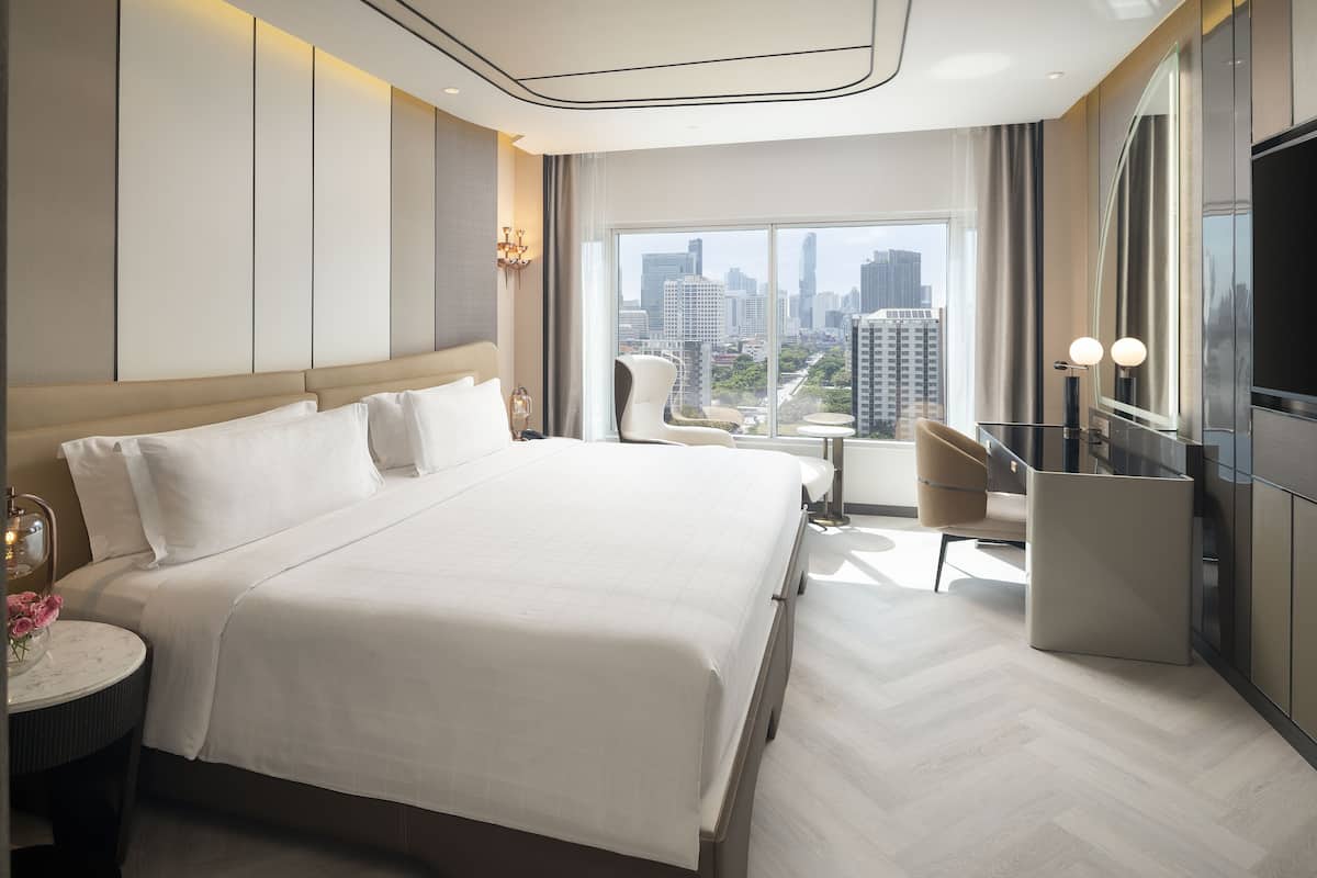 A modern hotel room with a large bed, a desk, and a view of the cityscape.