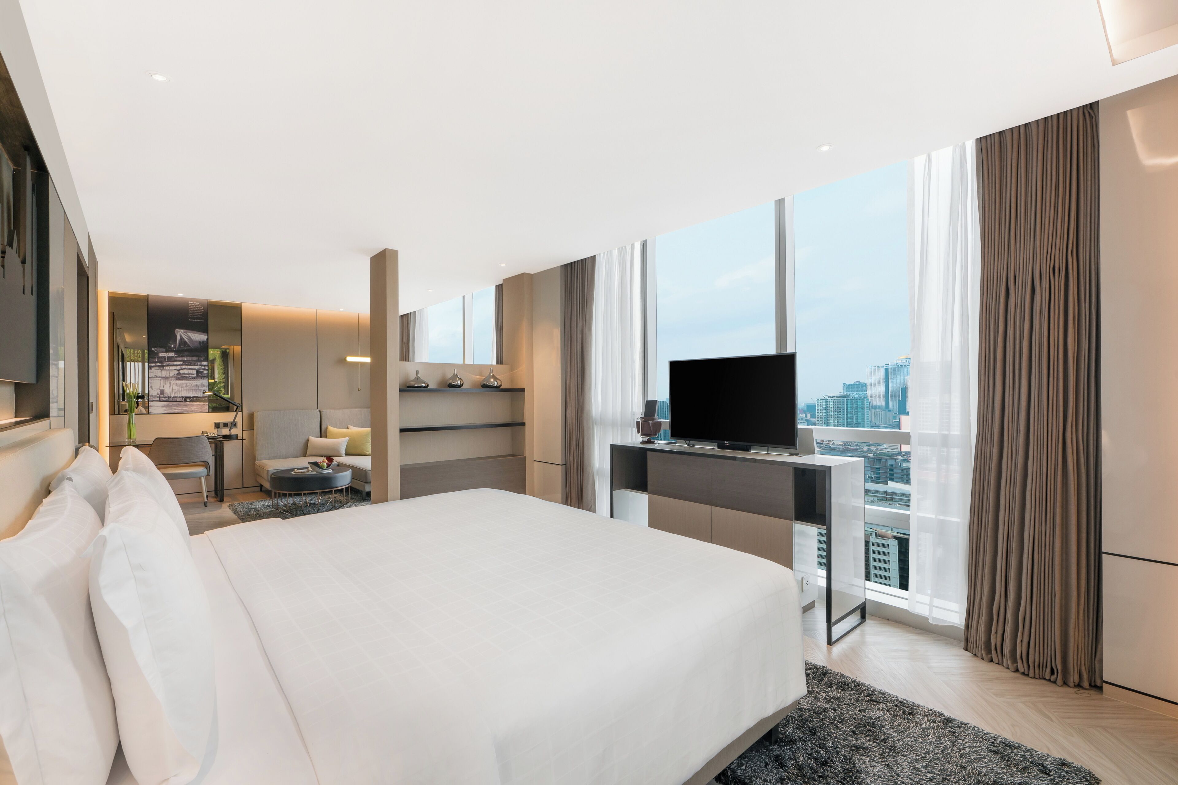 Ein modernes Hotelzimmer mit einem großen Bett, einem Schreibtisch, einem Flachbildfernseher, einer Sitzecke und Blick auf die Stadt.