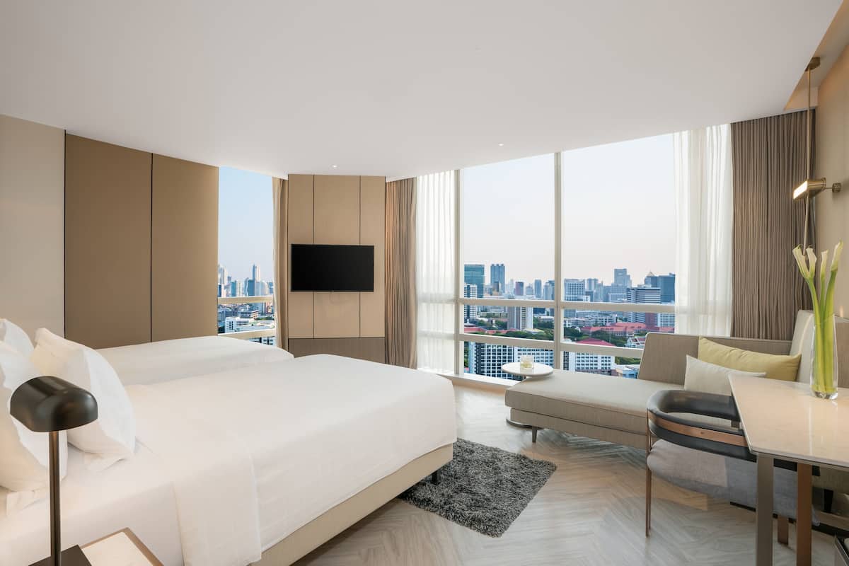 A hotel room with a bed, a desk, a chair, a TV, and a view of a cityscape.