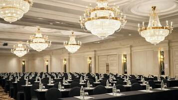 Un salón de banquetes con varias mesas, manteles negros y candelabros dorados.