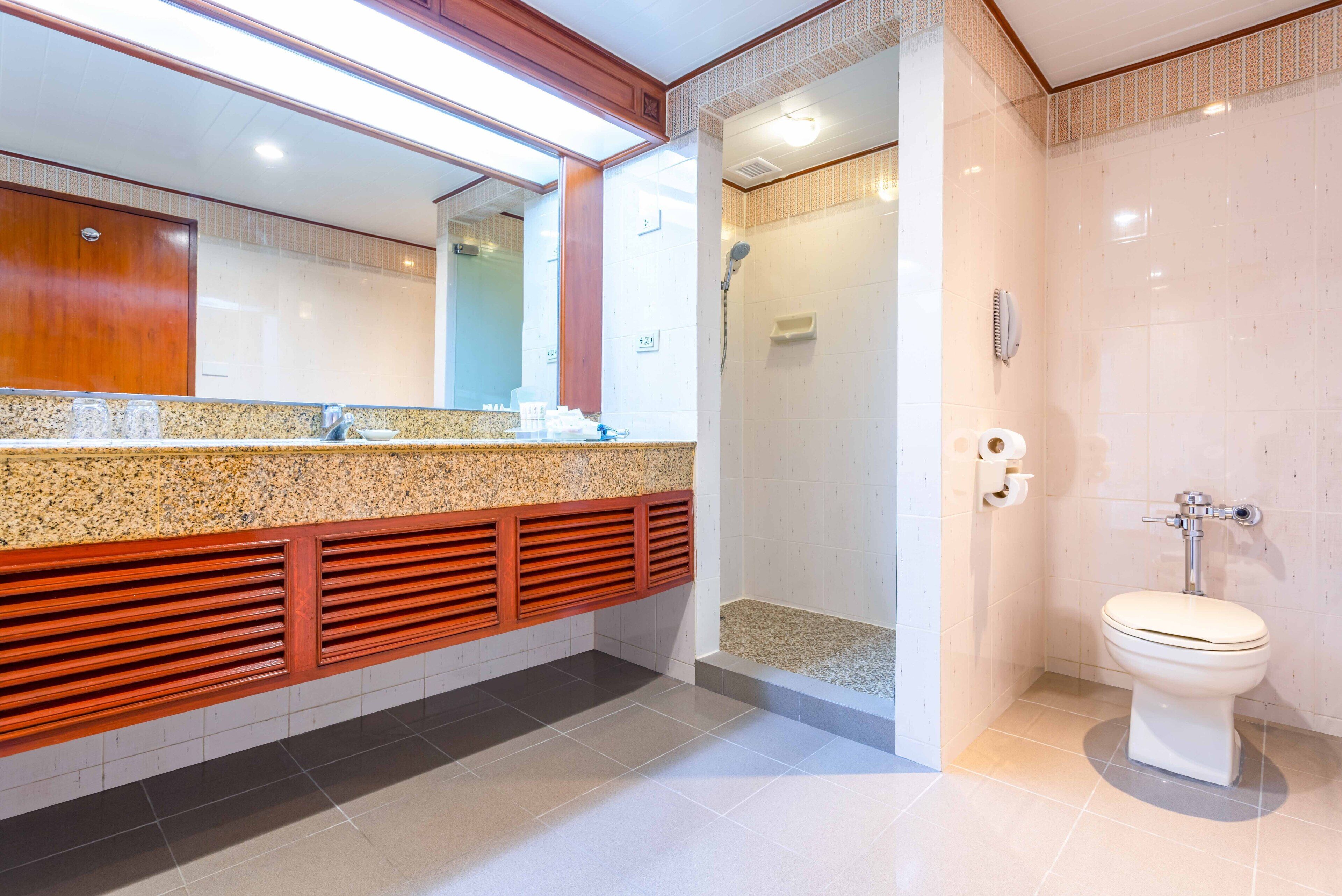 Un bagno moderno con un piano in granito, un mobile contenitore in legno, una doccia e un water.