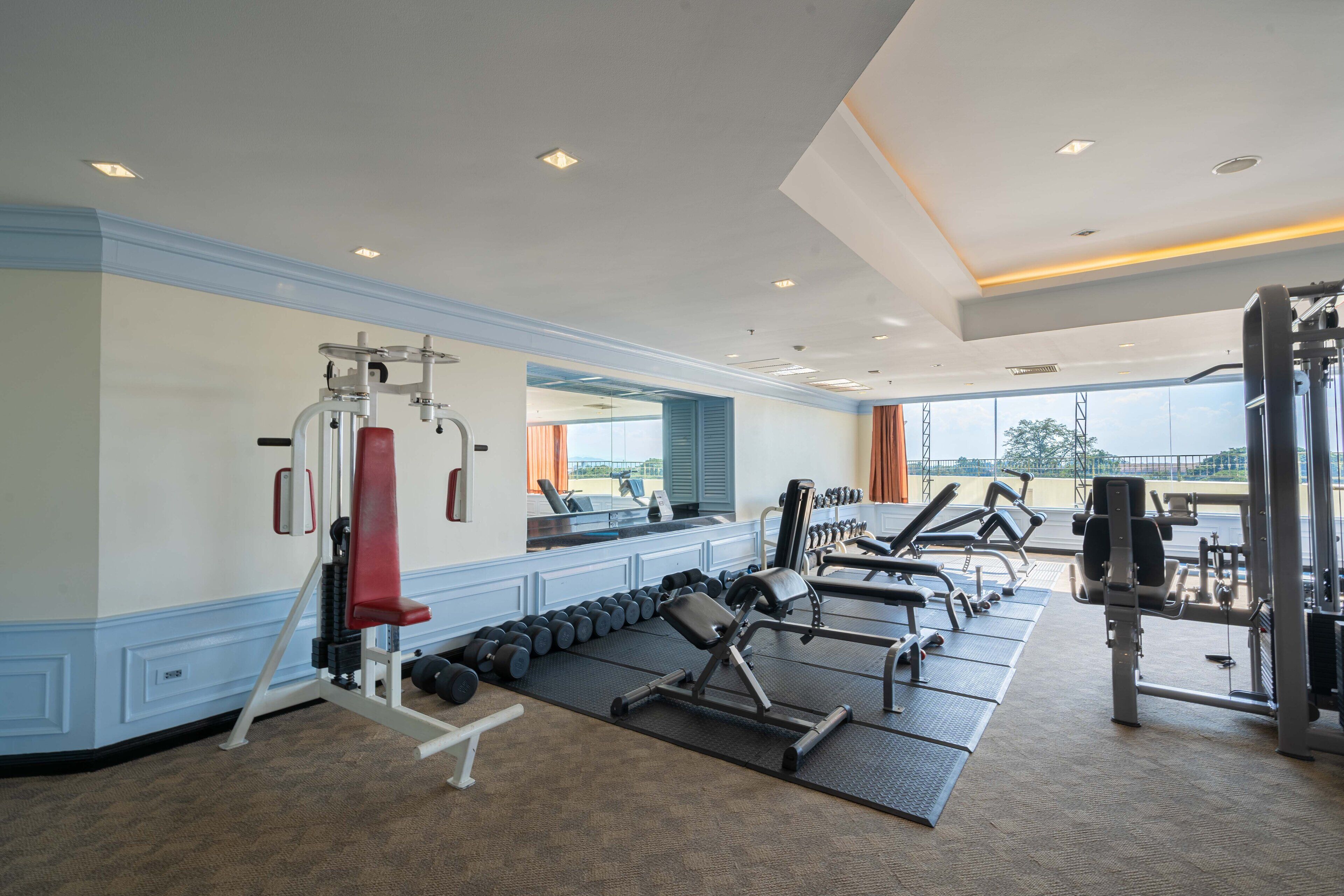 Un gimnasio con diferentes equipos de ejercicio, un espejo y vistas al exterior.