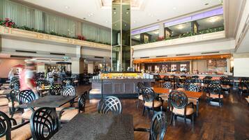 A spacious hotel lobby with multiple dining areas, a central bar, and a high ceiling with decorative elements.
