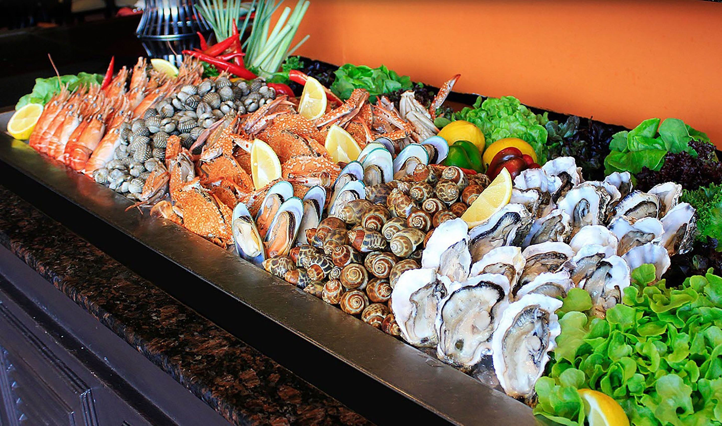 A seafood display with various shellfish and crustaceans, including oysters, clams, and crabs, arranged on a metal tray.