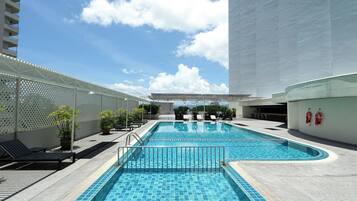 A swimming pool with lounge chairs and potted plants, surrounded by a white building.
