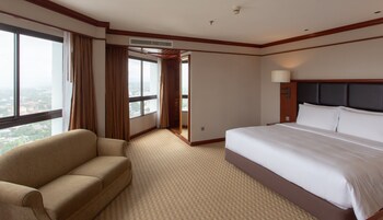A hotel room with a large bed, a sofa, a window with curtains, and an air conditioning unit.