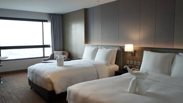 A hotel room with two beds, a desk, a chair, and a window with curtains.