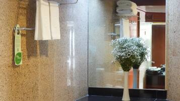 A bathroom with a granite countertop, a white bathtub, a mirror, and a flower vase.