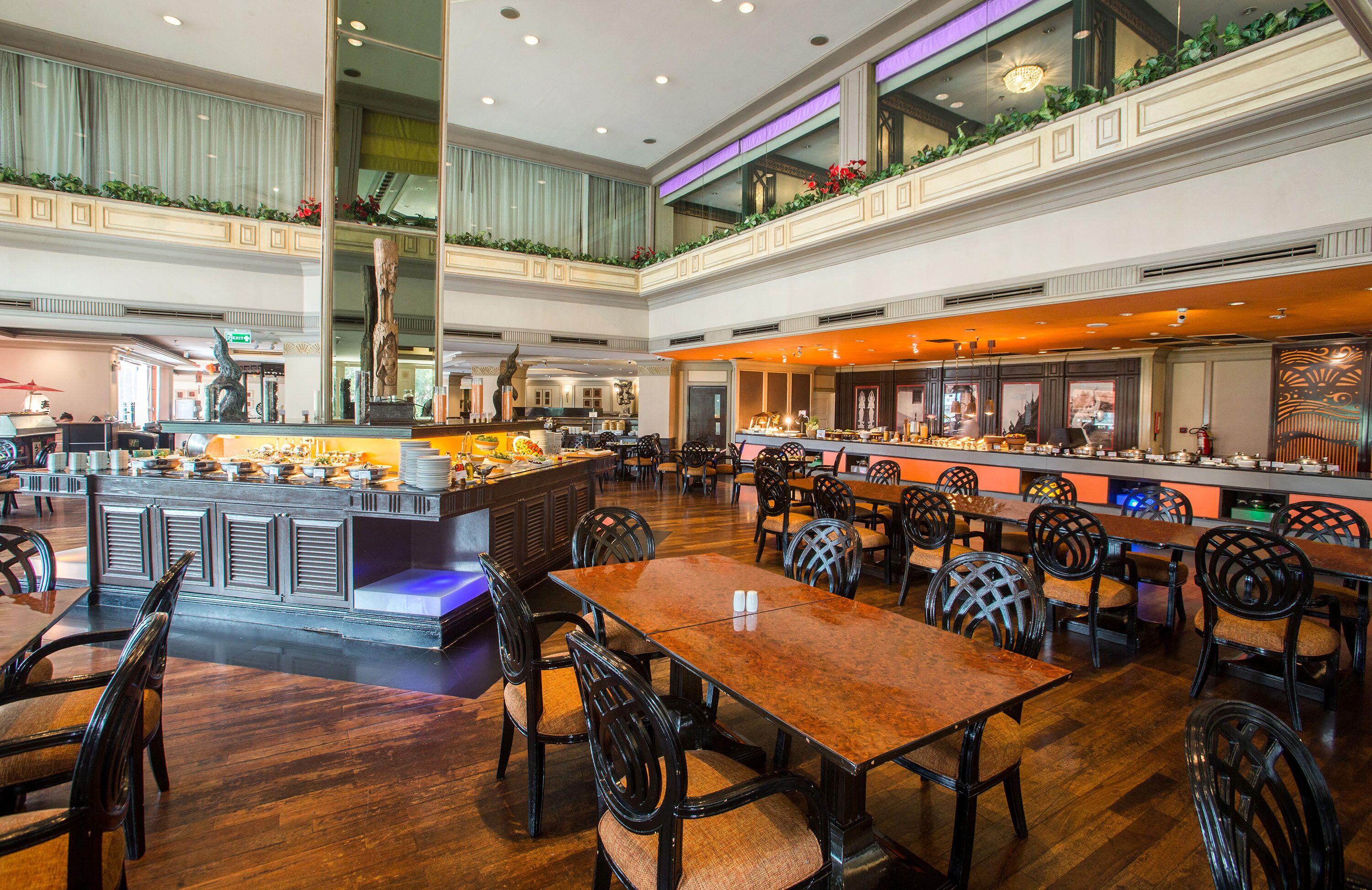 A spacious hotel lobby with multiple dining areas, a central bar, and a high ceiling with decorative lighting.