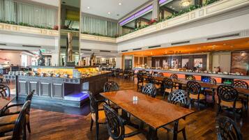 A spacious hotel lobby with multiple dining areas, a central bar, and a high ceiling with decorative lighting.