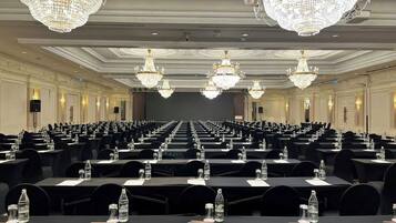Un salón de conferencias con filas de mesas, sillas negras, botellas de agua y candelabros.