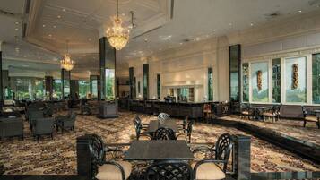 A spacious hotel lobby with a patterned carpet, multiple seating areas, a bar, and large windows offering views.