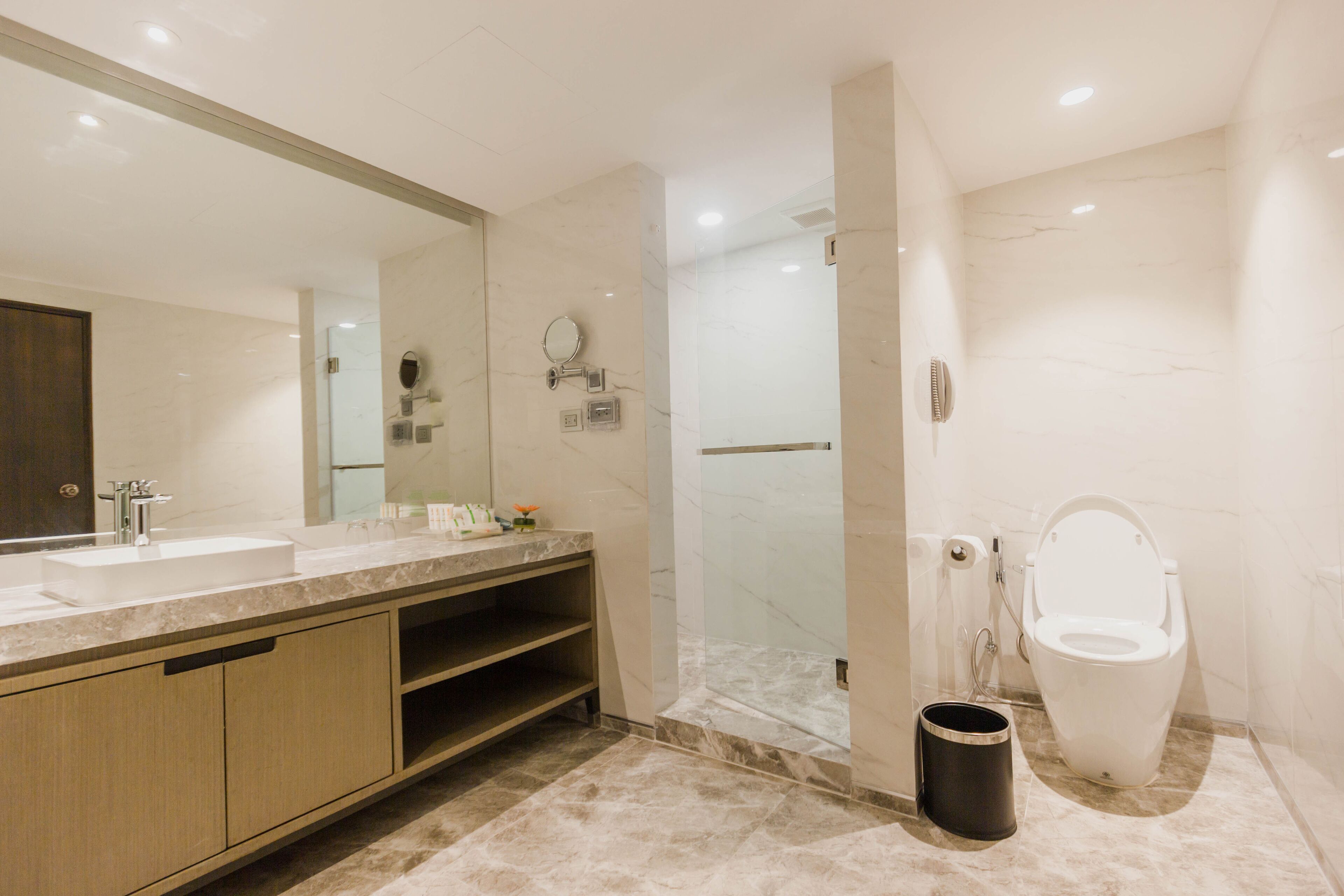 A modern bathroom with a large mirror, two sinks, a shower enclosure, and a toilet.
