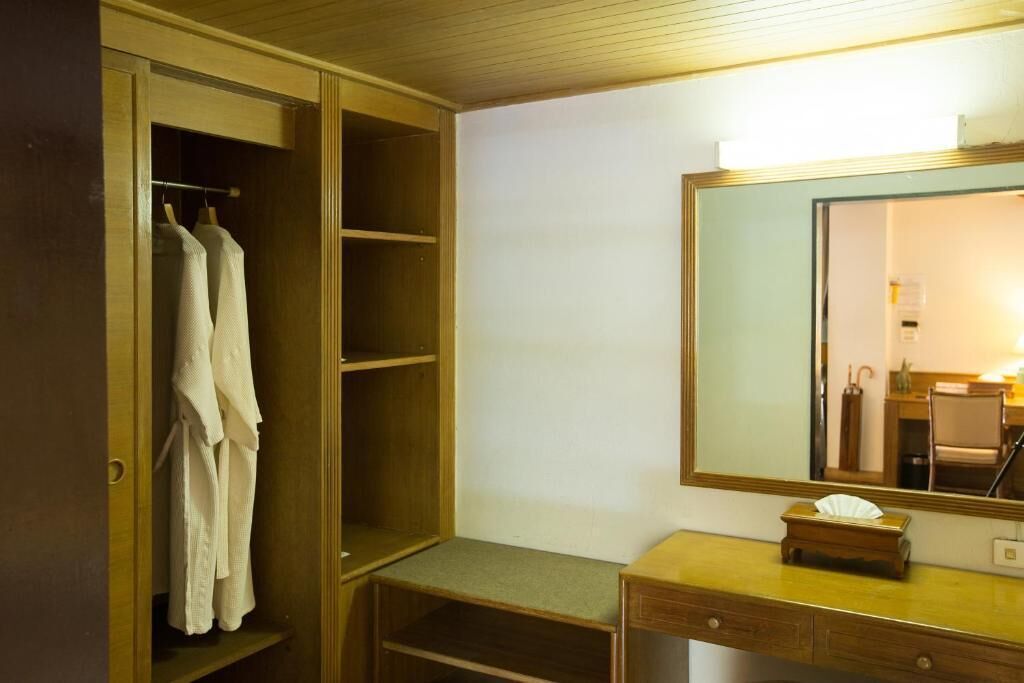 A wooden wardrobe with hanging robes, a mirror, and a small wooden stool with a tissue box.