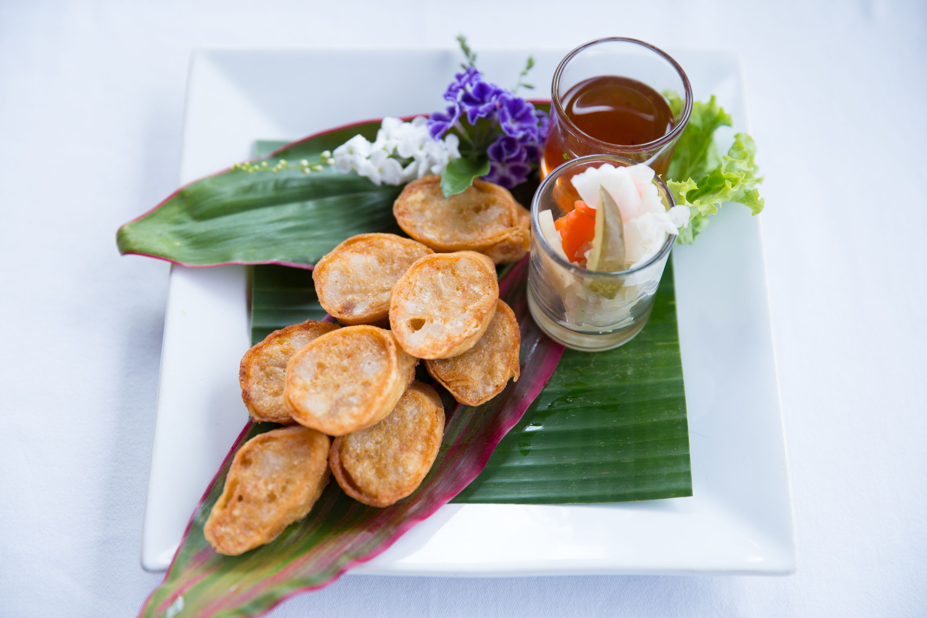 A plate of fried snacks and a small glass of sauce on a white plate with a green leaf.