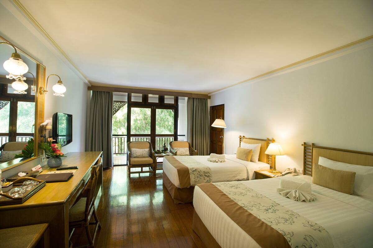 Ein Hotelzimmer mit zwei Betten, einem Schreibtisch, einem Stuhl, einer Lampe und einem großen Fenster mit Vorhängen.