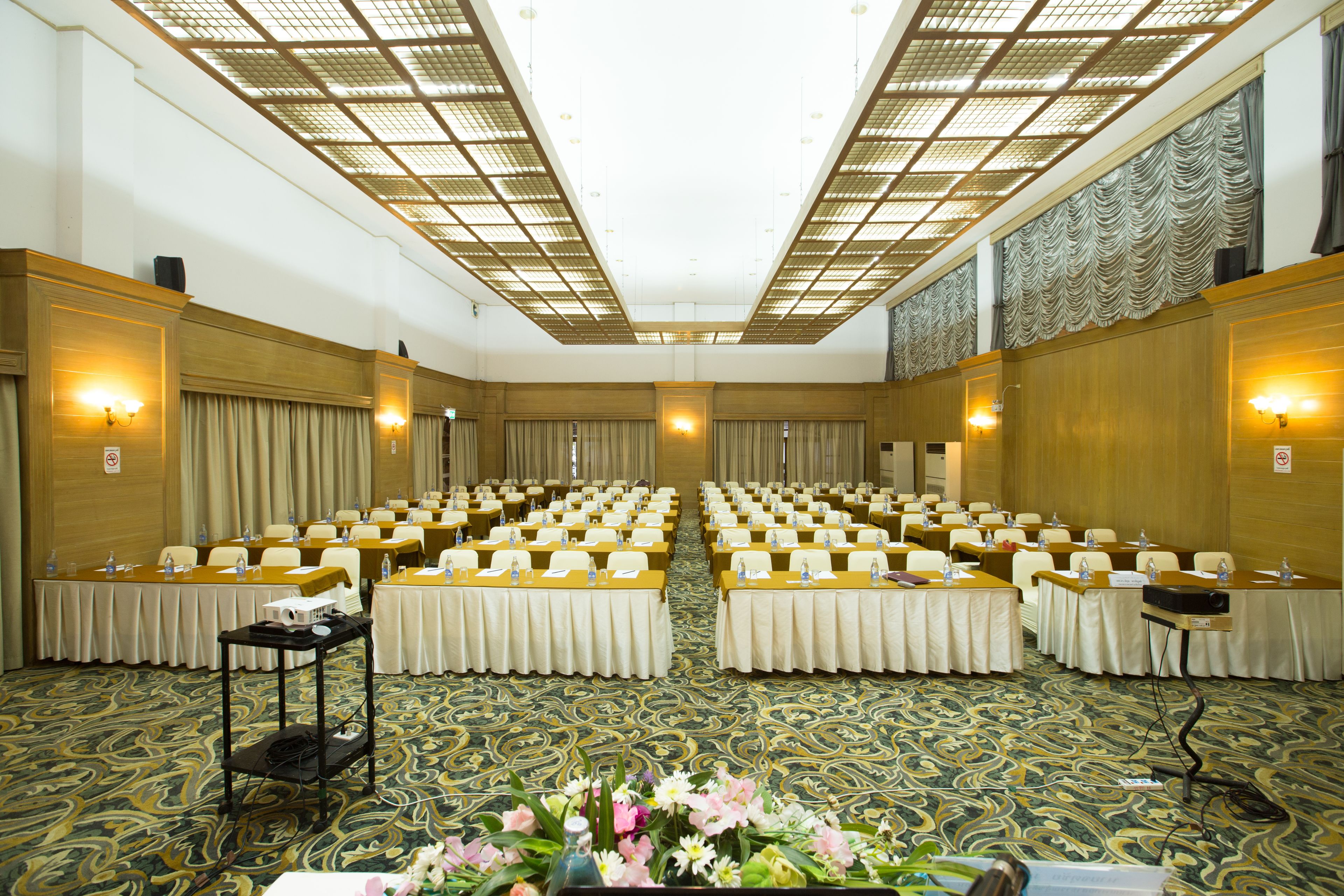 A conference room with rows of tables, a floral arrangement, and a patterned carpet.