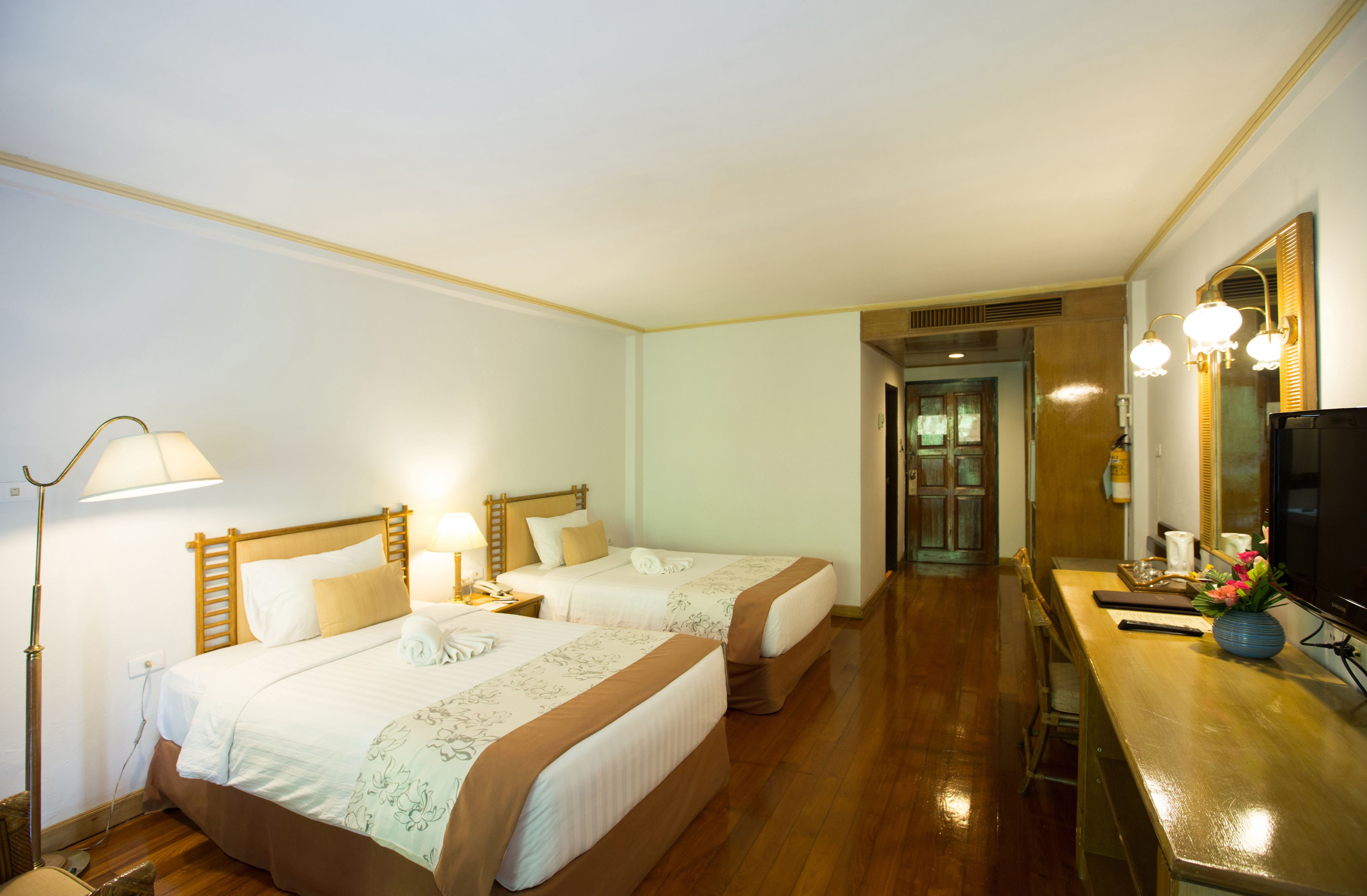 Een hotelkamer met twee bedden, een bureau met een televisie en een zichtbare badkamer door een geopende deur.