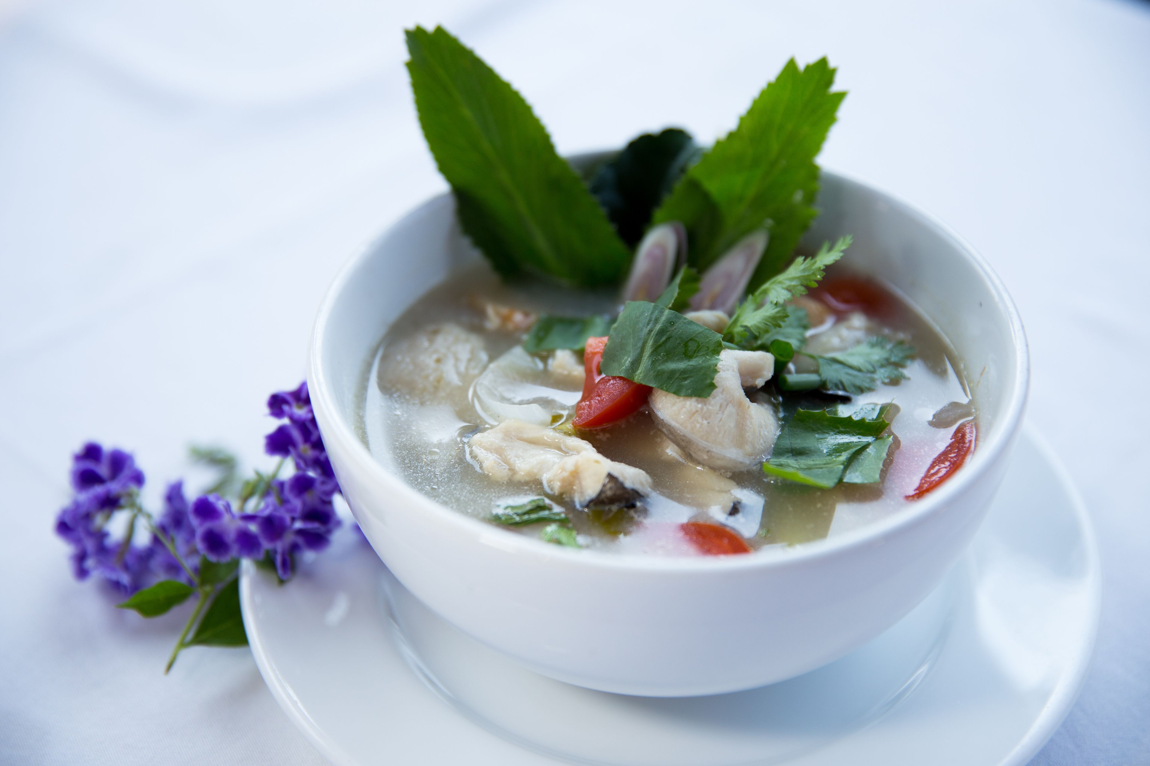 A bowl of soup with various ingredients, including herbs and vegetables, on a white plate.