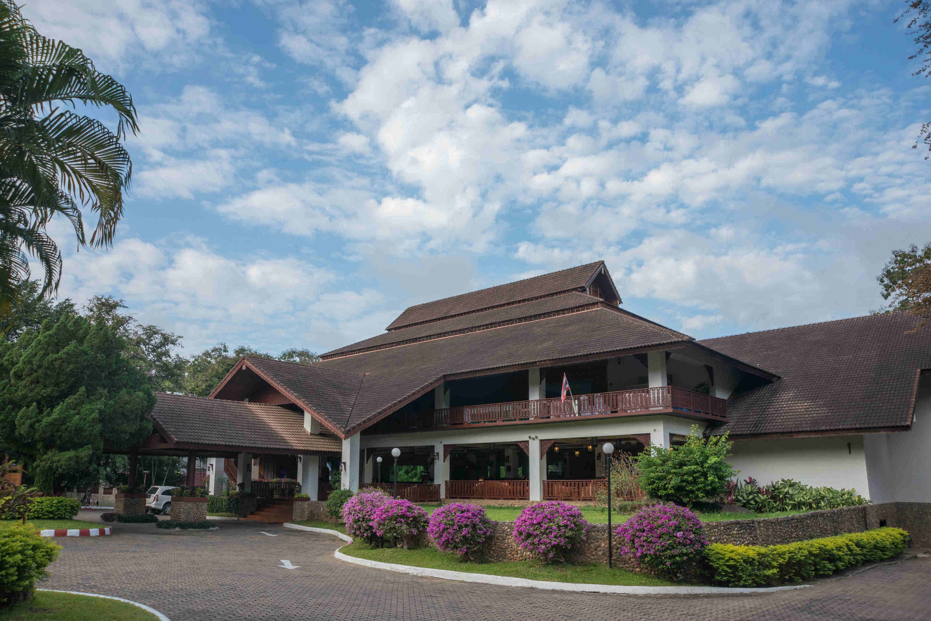 A two-story building with a balcony, surrounded by well-maintained gardens and a paved driveway.