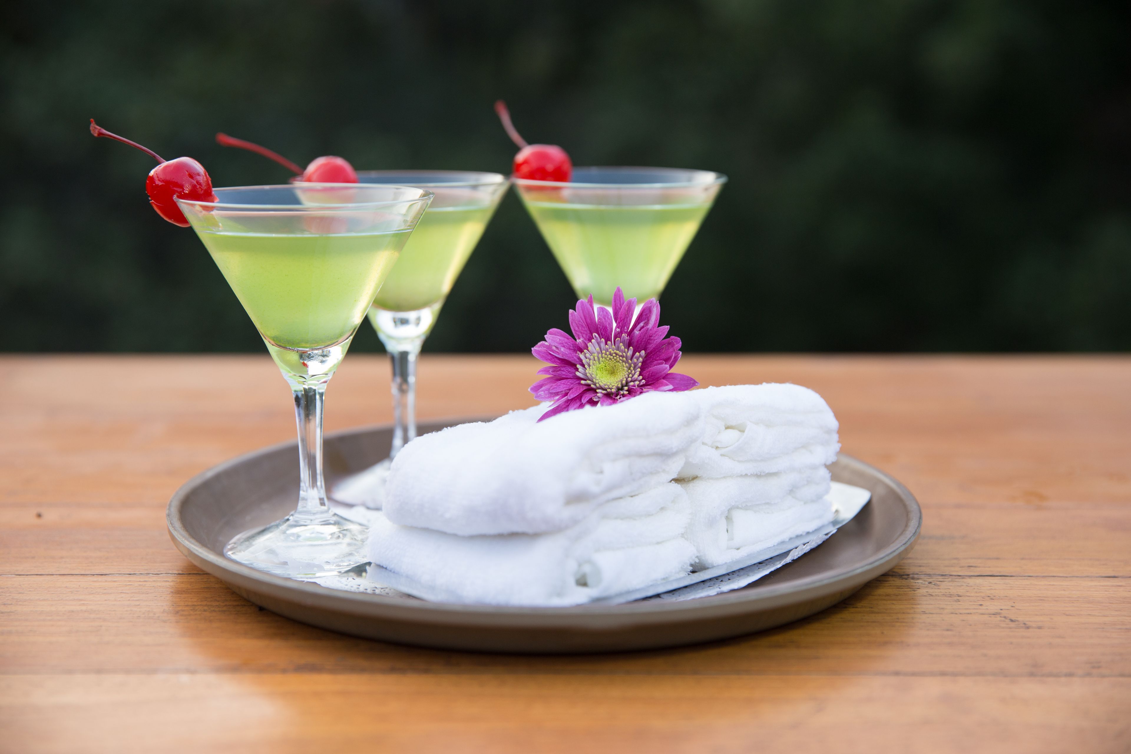 A tray with two martini glasses, each with a cherry, and a plate of folded towels with a purple flower.