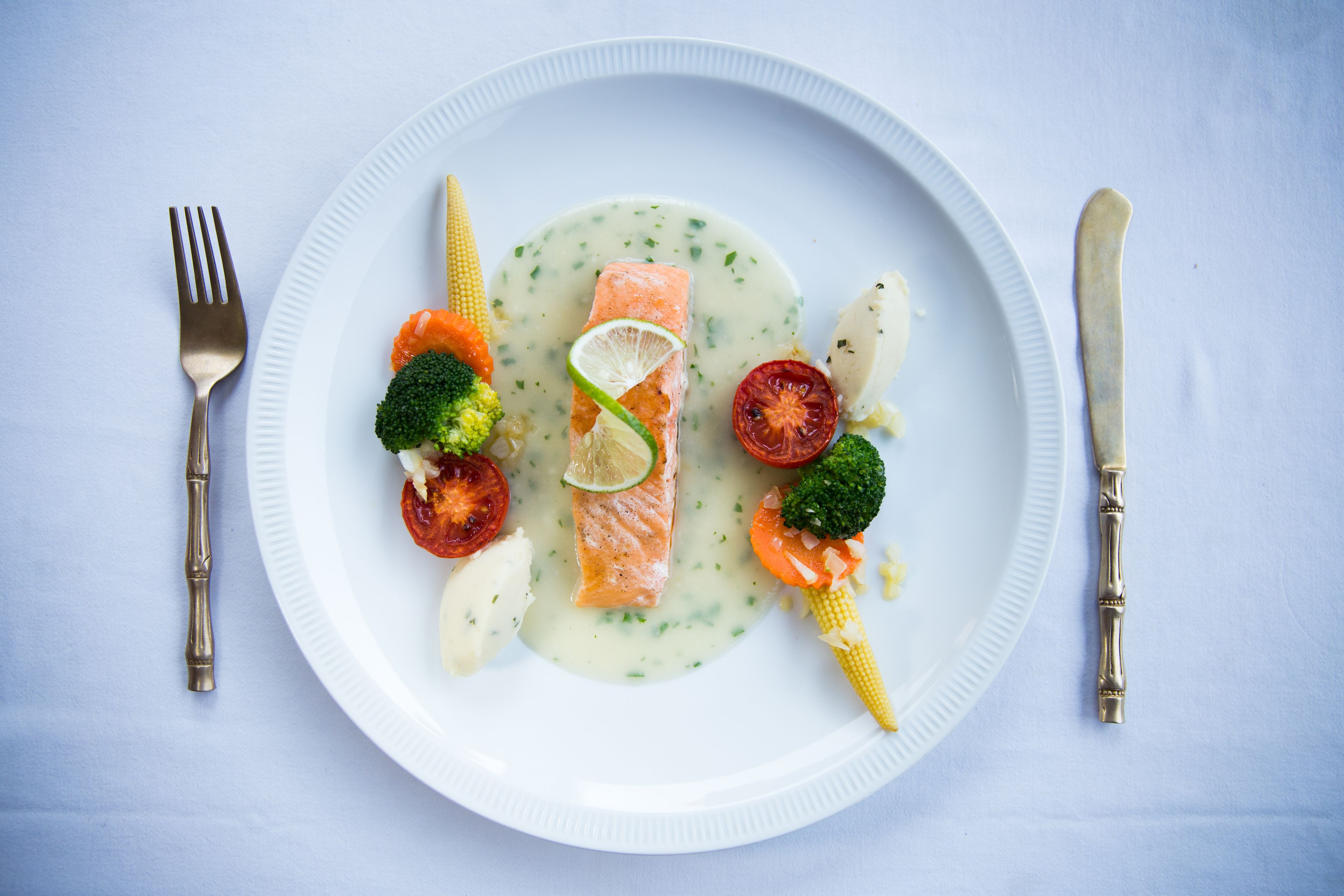 A plate of food with salmon, vegetables, and a creamy sauce.