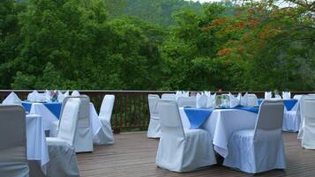 Un área de comedor al aire libre con mesas y sillas cubiertas con manteles blancos.