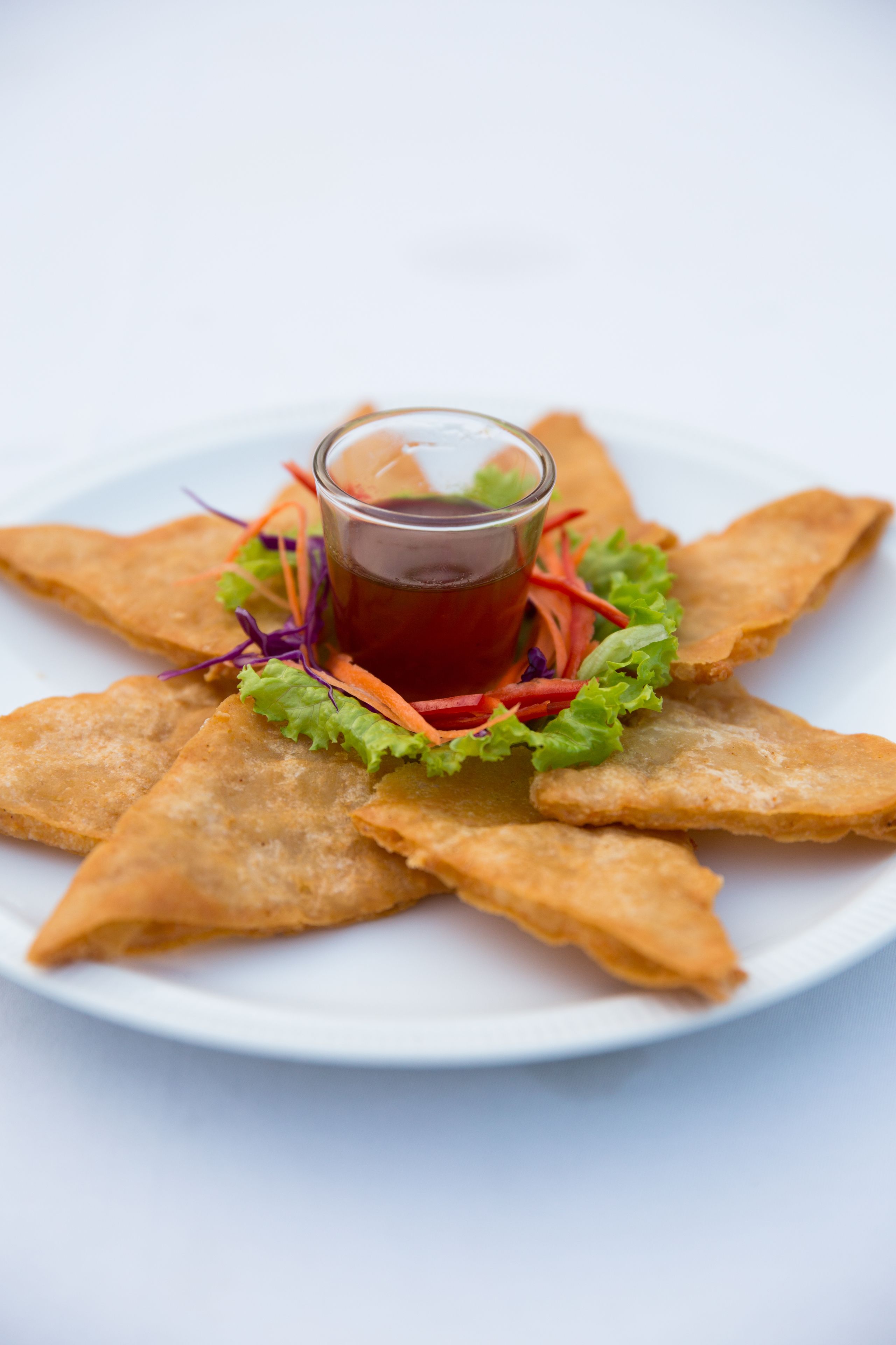 Une assiette de petits chaussons frits en forme de triangle, accompagnés d’une sauce rouge et d’une salade.