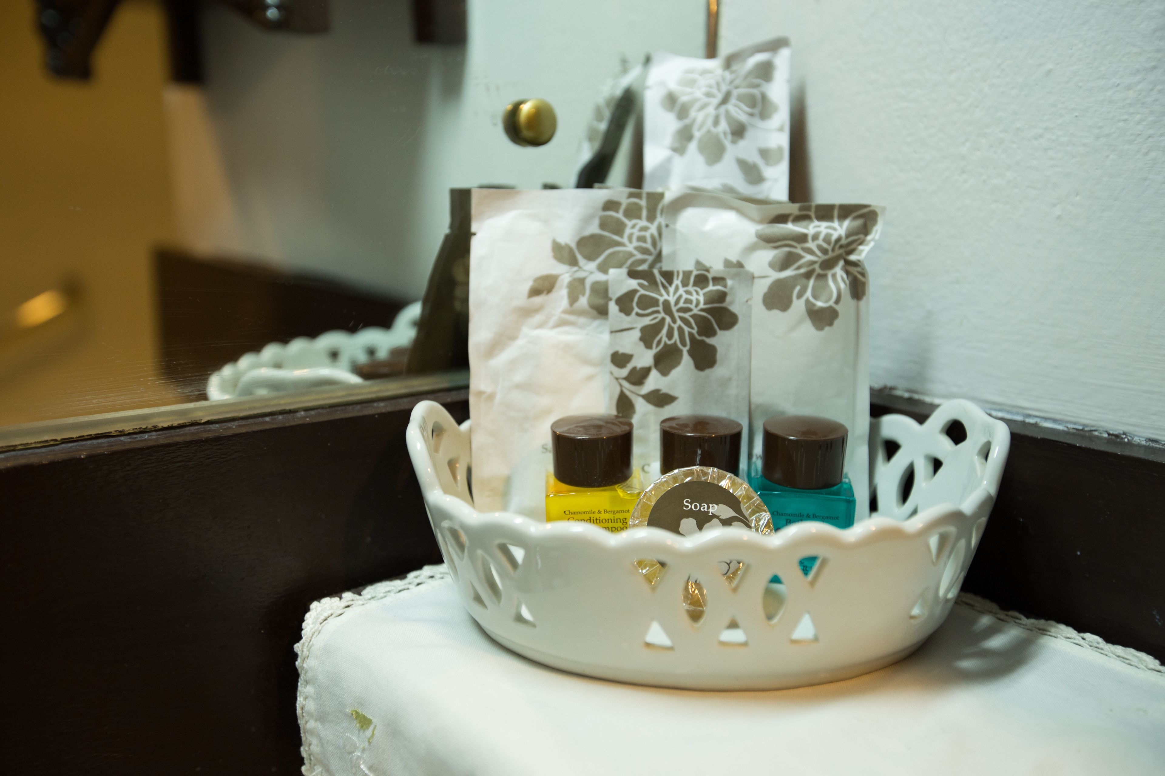 A white decorative basket with floral patterns containing toiletries like soap and lotion.