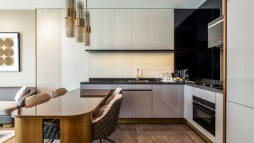 A modern kitchen with a dining area, featuring a wooden table, cushioned chairs, and a pendant light.