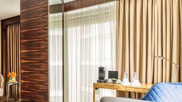 A modern hotel room with a wooden accent wall, a glass partition, a wooden desk with a coffee maker, and a blue chair.