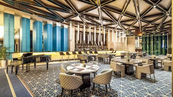 A modern hotel lobby with a geometric patterned floor, a bar area, and a seating arrangement with round tables and cushioned chairs.