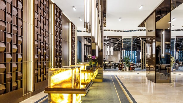 Un moderno vestíbulo de hotel con un mostrador de recepción, zona de estar y un espejo grande que refleja el interior.