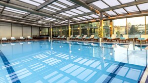 Una piscina interior con agua cristalina, sillas de descanso y techo de vidrio.