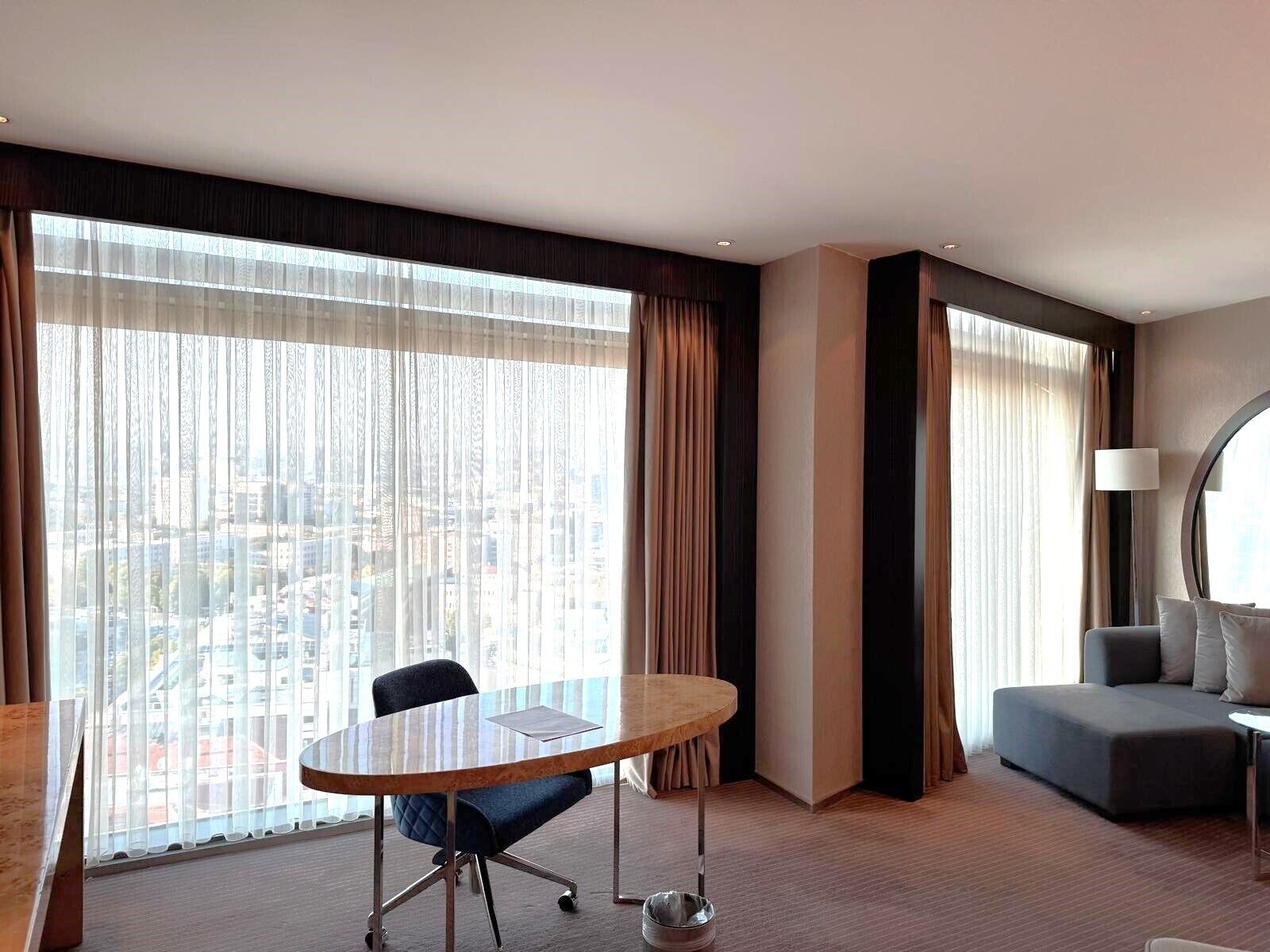 Habitación de hotel con un ventanal grande, una mesa redonda, un sofá y una lámpara.