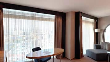 Habitación de hotel con un ventanal grande, una mesa redonda, un sofá y una lámpara.