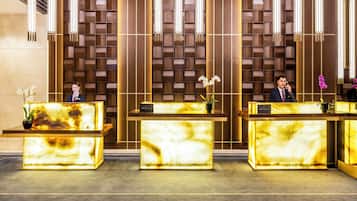 A reception area with three reception desks, each with a marble top and a plant on the left side.