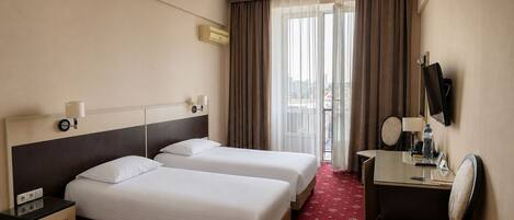 A hotel room with two beds, a desk with a chair, a TV, and a window with curtains.