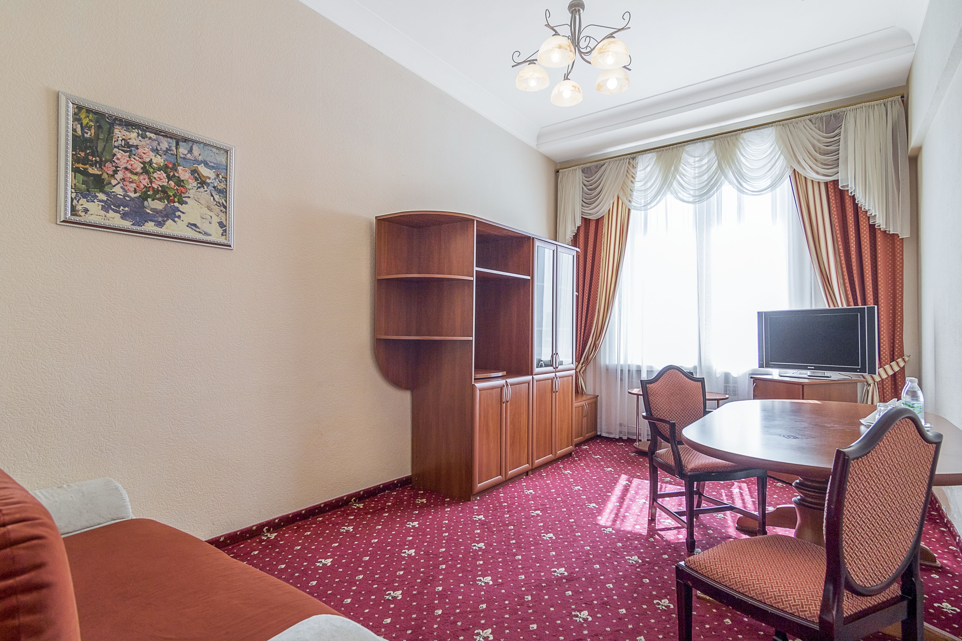 Ein Hotelzimmer mit Esstisch, Stühlen, Fernseher, Bücherregal und einem Gemälde an der Wand.