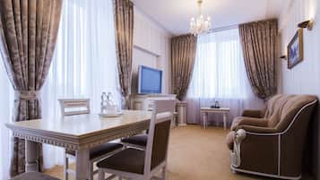 Quarto de hotel com uma mesa de jantar, duas cadeiras, uma televisão, um sofá e uma mesinha lateral.