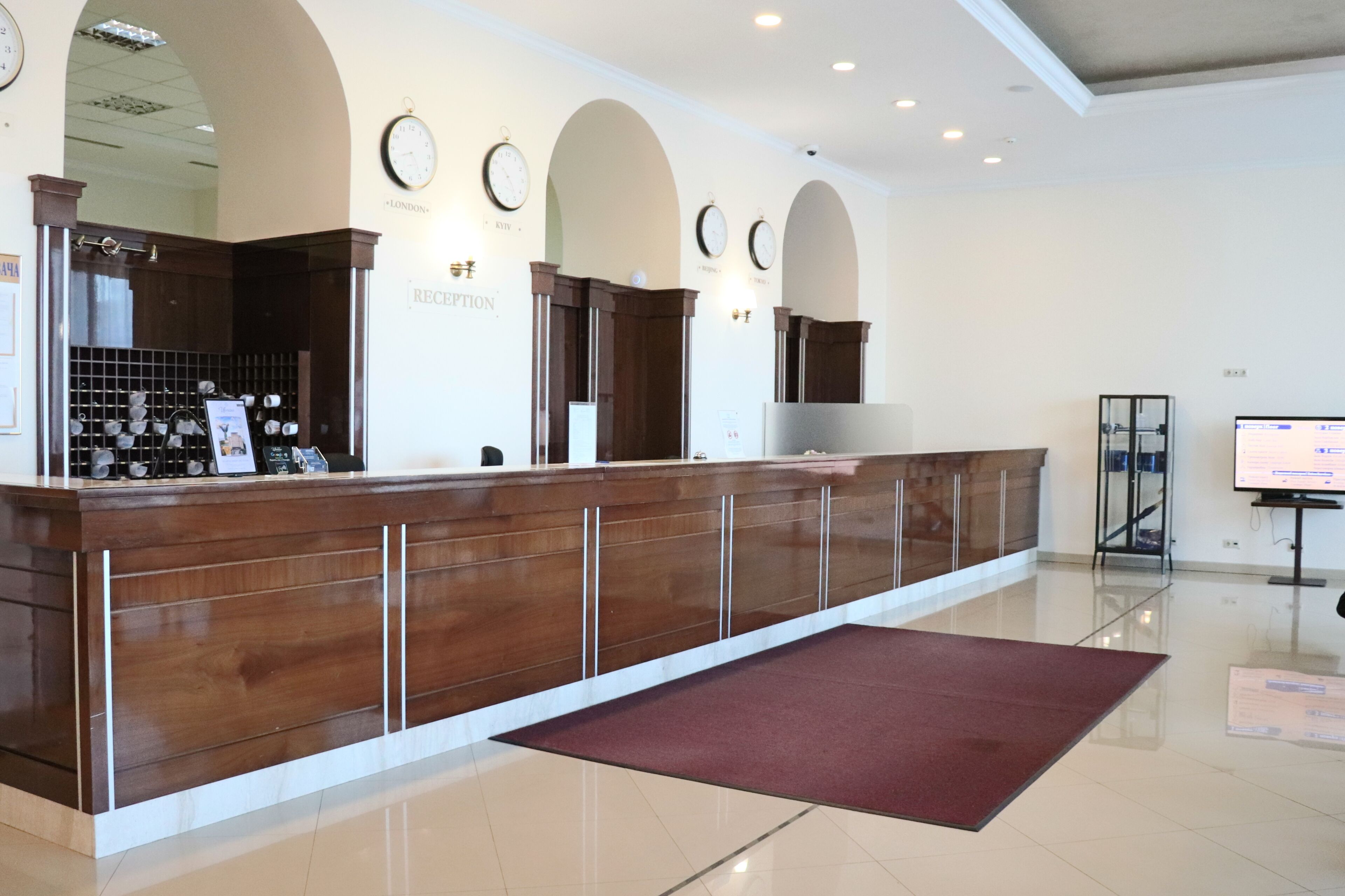 A reception area with a wooden reception desk, a red carpet, and a wall with clocks.