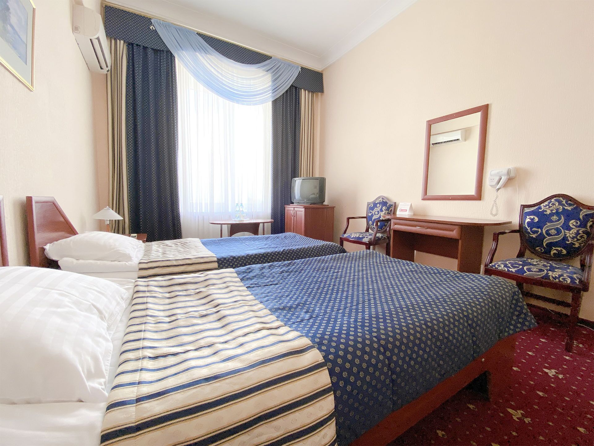 A hotel room with two beds, a desk, a chair, a television, and a mirror.
