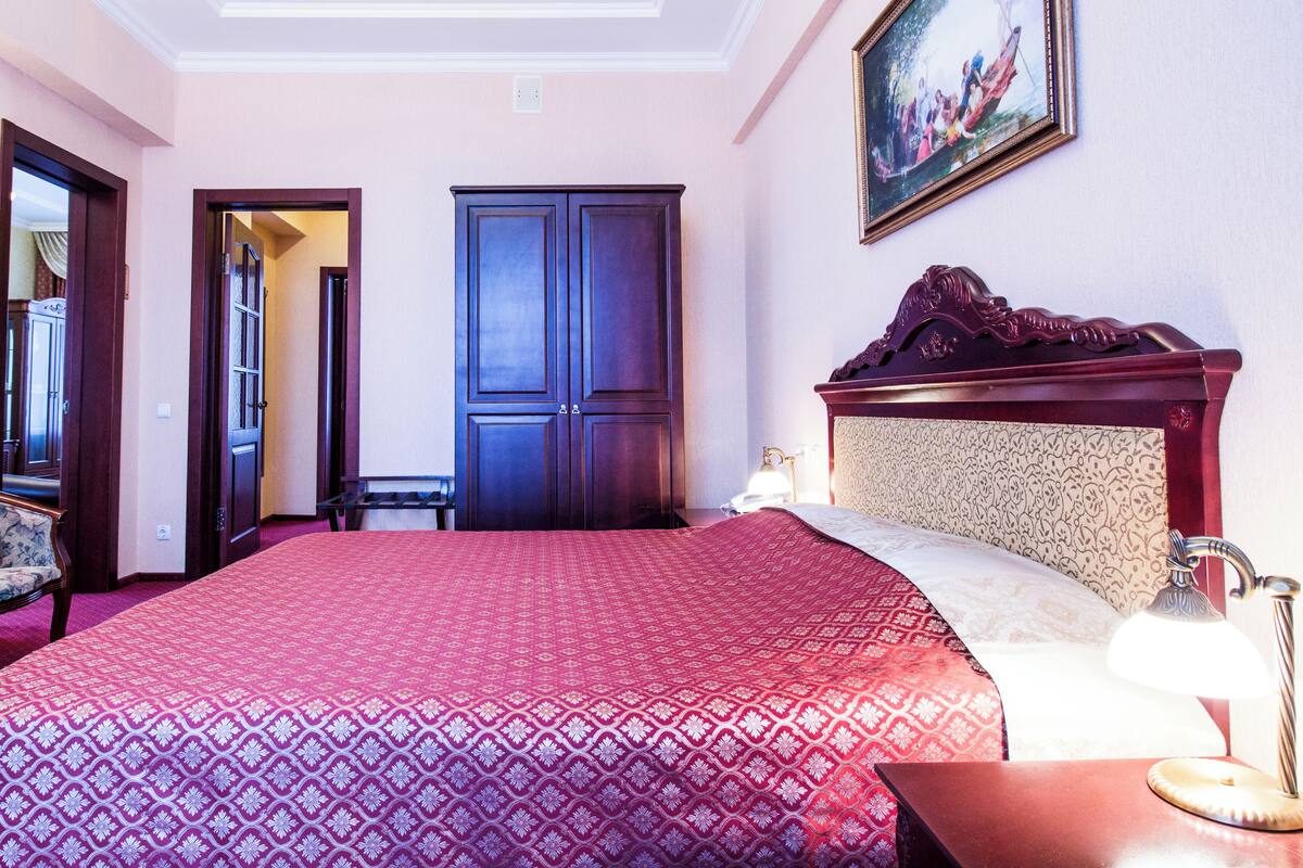 Una habitación de hotel con una cama grande, un armario de madera, una silla y un cuadro en la pared.